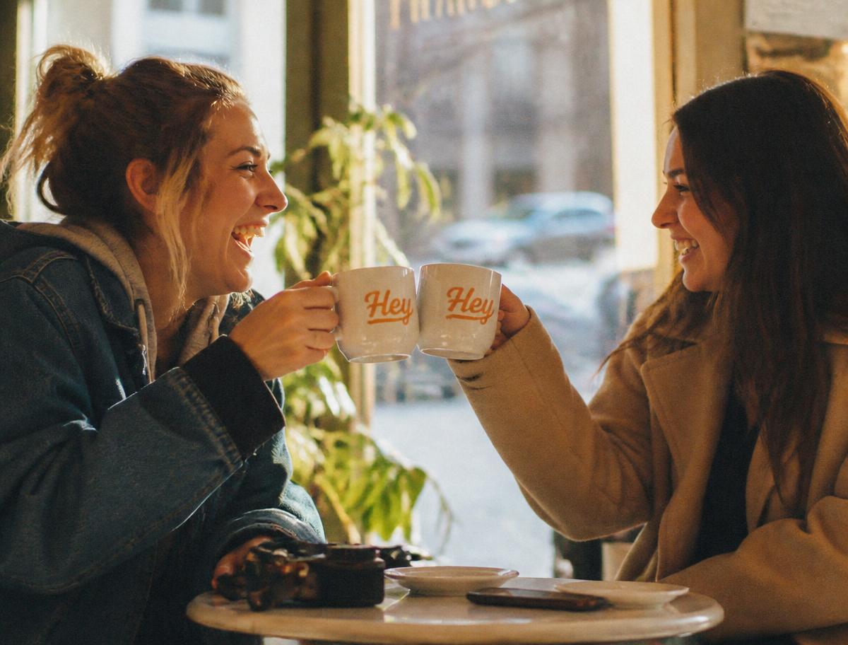 A HeyThere consultation across a wooden table — two Hey-branded coffee mugs, an open notebook, and a calendar